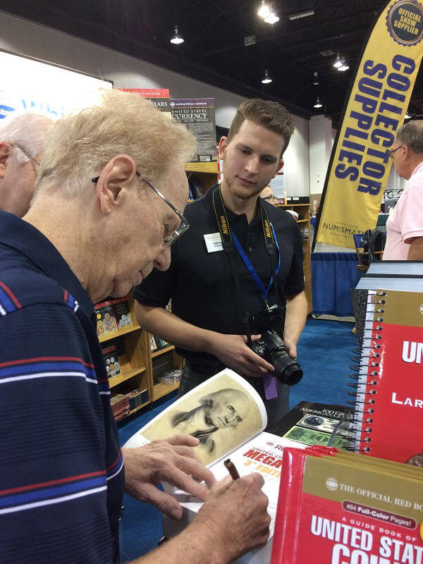 Kenneth Bressett autographing a copy of the 1,504-page Mega Red for Caleb Noel, then news editor (and now editor) of The Numismatist, the magazine of the American Numismatic Association. (2017).